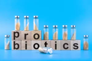 Sklenené ampulky s práškom a drevené kocky s nápisom „probiotics“ na modrom pozadí – moderná ilustrácia probiotík v kontexte zdravia čriev.