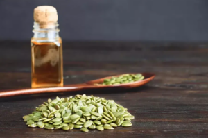 Tekvicové semienka a fľaštička s olejom na drevenom stole – prírodné liečivé rastliny s antiparazitárnym účinkom.