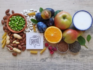 Rôzne potraviny bohaté na beta-glukán, ako zelenina, ovocie, orechy, strukoviny, semienka a jogurt, zoradené na stole spolu s ilustráciou čreva – symbolizujúc účinky beta-glukánu na zdravie tráviaceho systému a podporu imunity.