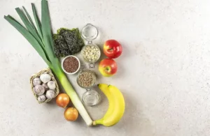 Čerstvé prebiotické potraviny: pór, cesnak, cibuľa, jablká, banán, ovsené vločky a semienka zoradené na svetlom podklade – prirodzené zdroje prebiotík pre zdravú črevnú flóru.