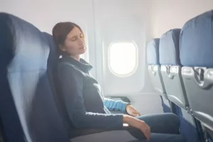 Žena sedí pohodlne v lietadle pri okne s opretou hlavou a uvoľnenými rukami na podrúčkach – ilustračný obrázok súvisiaci s nevoľnosťou pri cestovaní.