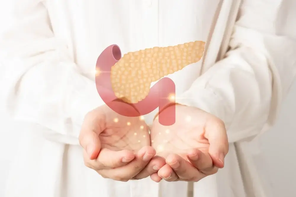 Osoba v bielom oblečení jemne drží v dlaniach digitálnu ilustráciu pankreasu so zvýraznenými bodmi – symbolizuje dôležitosť zdravia slinivky, jej anatomickú polohu a prevenciu ochorení.